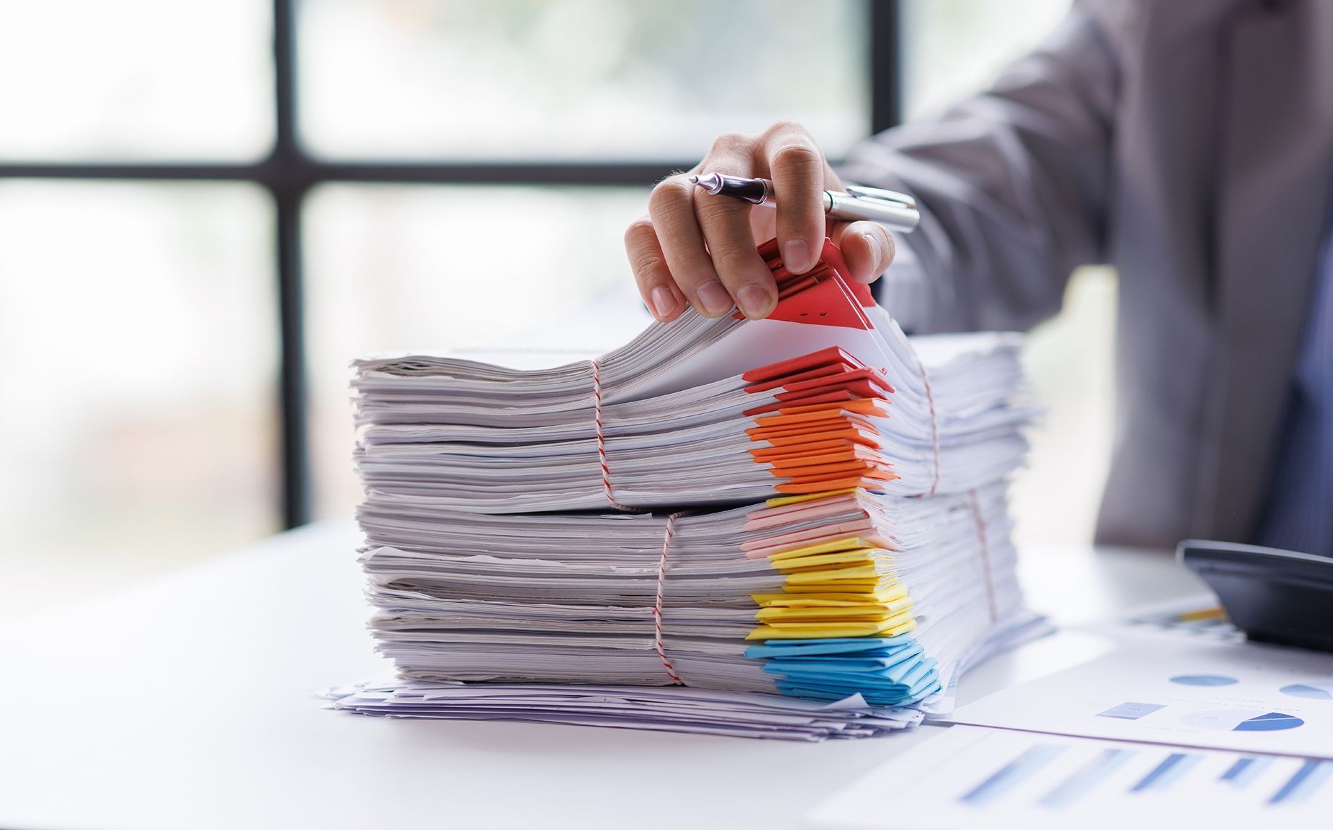A person is holding a pen over a stack of papers.
