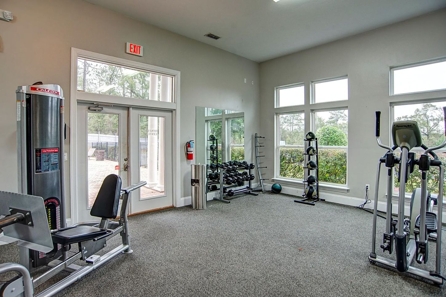 A gym with a lot of exercise equipment and a lot of windows.