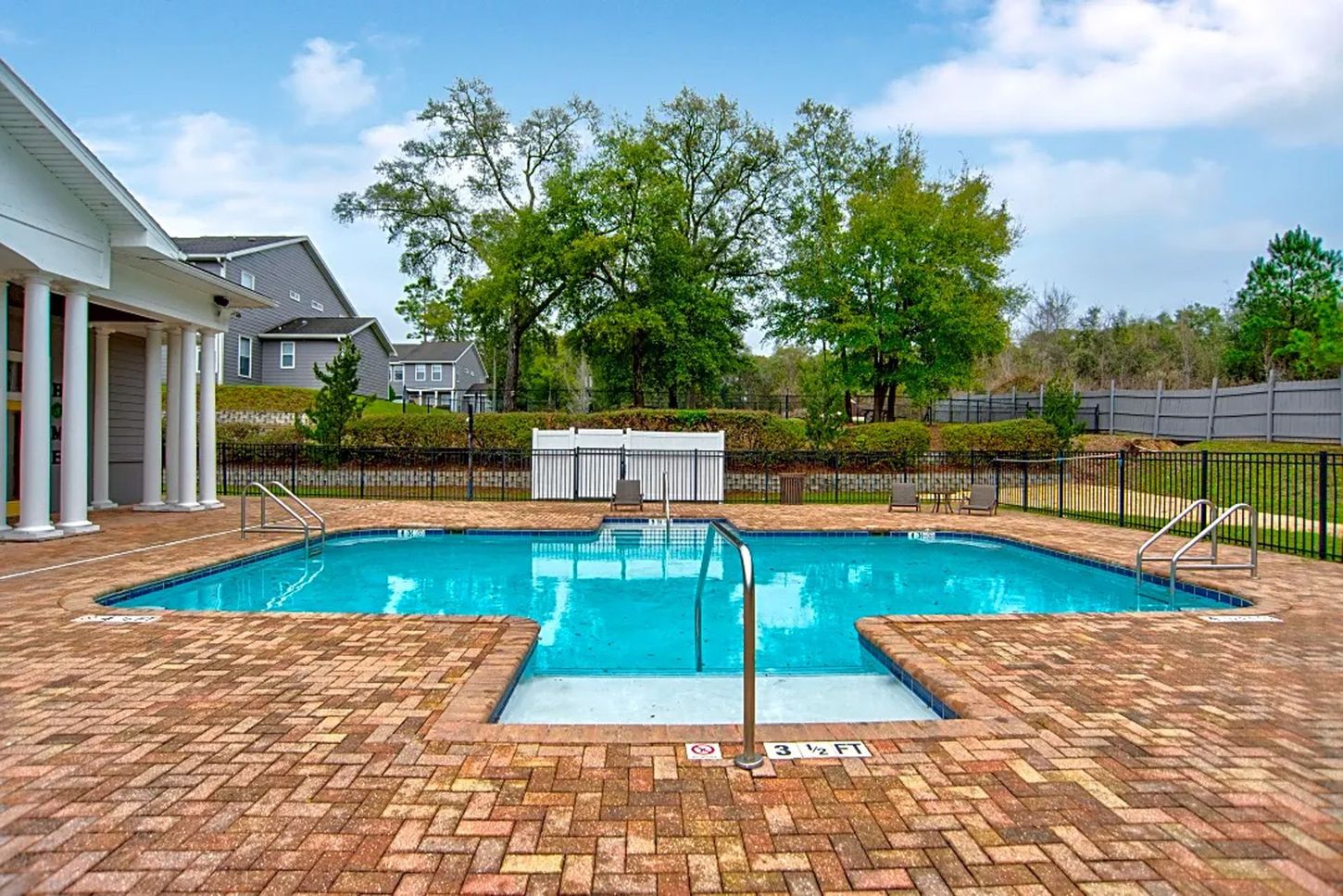 A large swimming pool is surrounded by a brick patio.