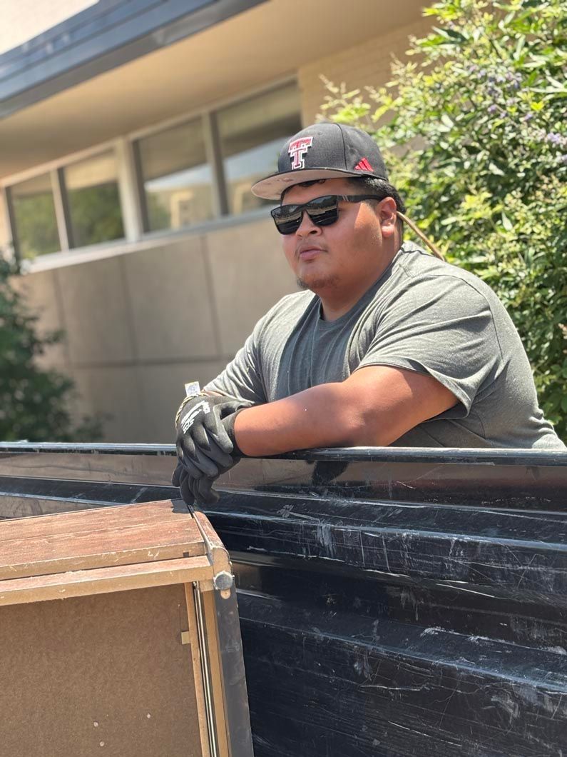 A man wearing a hat and sunglasses is sitting in the back of a truck.