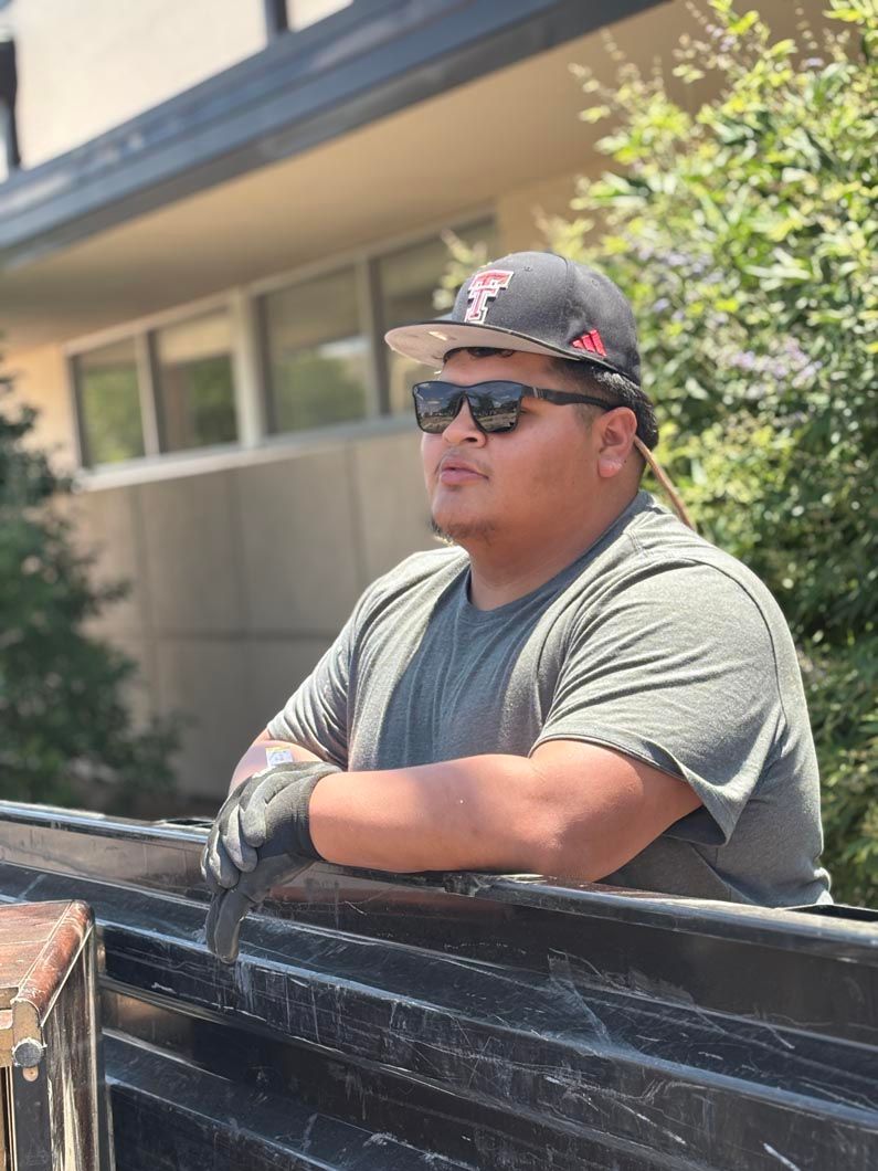 A man wearing sunglasses and a hat is leaning on the back of a truck.