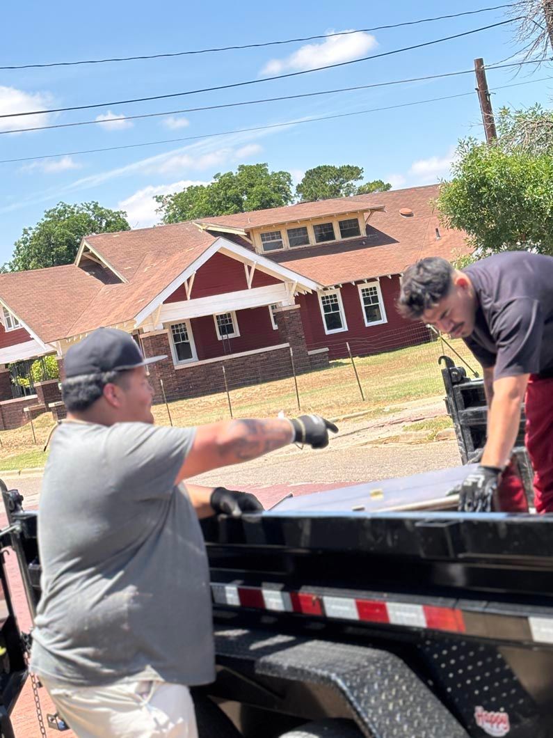 Two men are working on a trailer in front of a red house