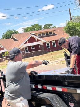 Two men are working on a trailer in front of a red house