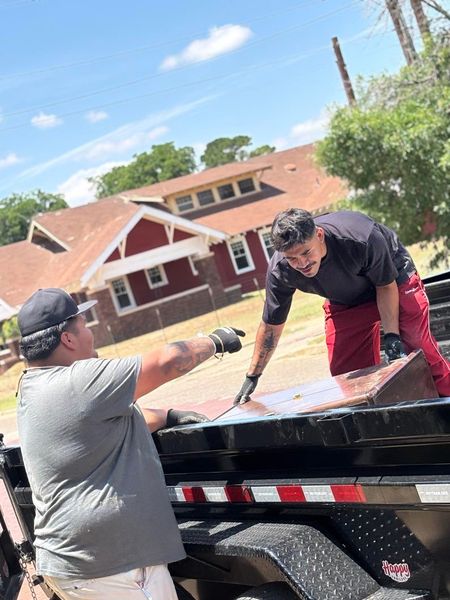 Two men are working on a trailer in front of a house.