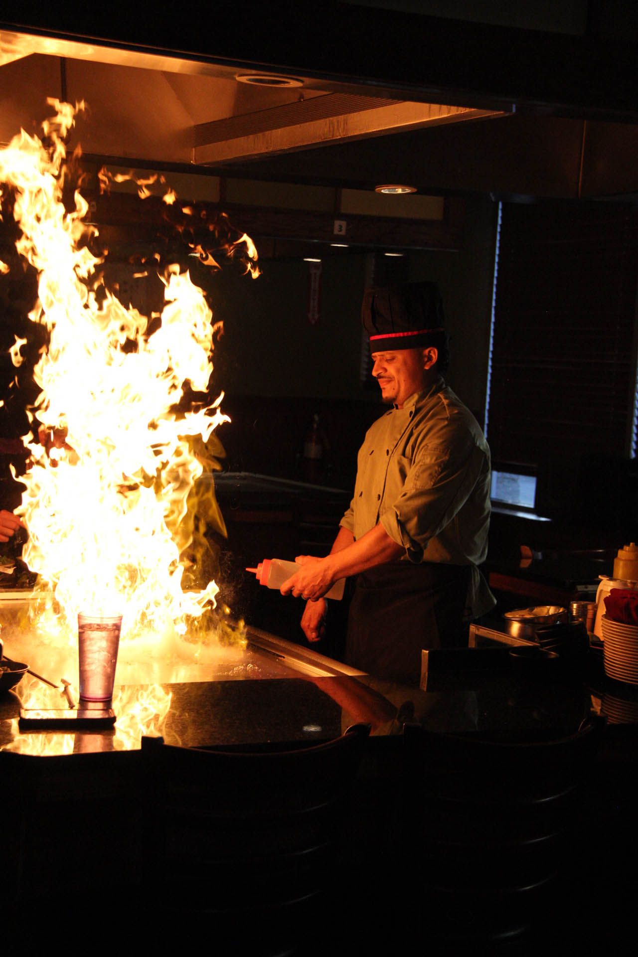 A chef is cooking food on a grill with flames coming out of it.