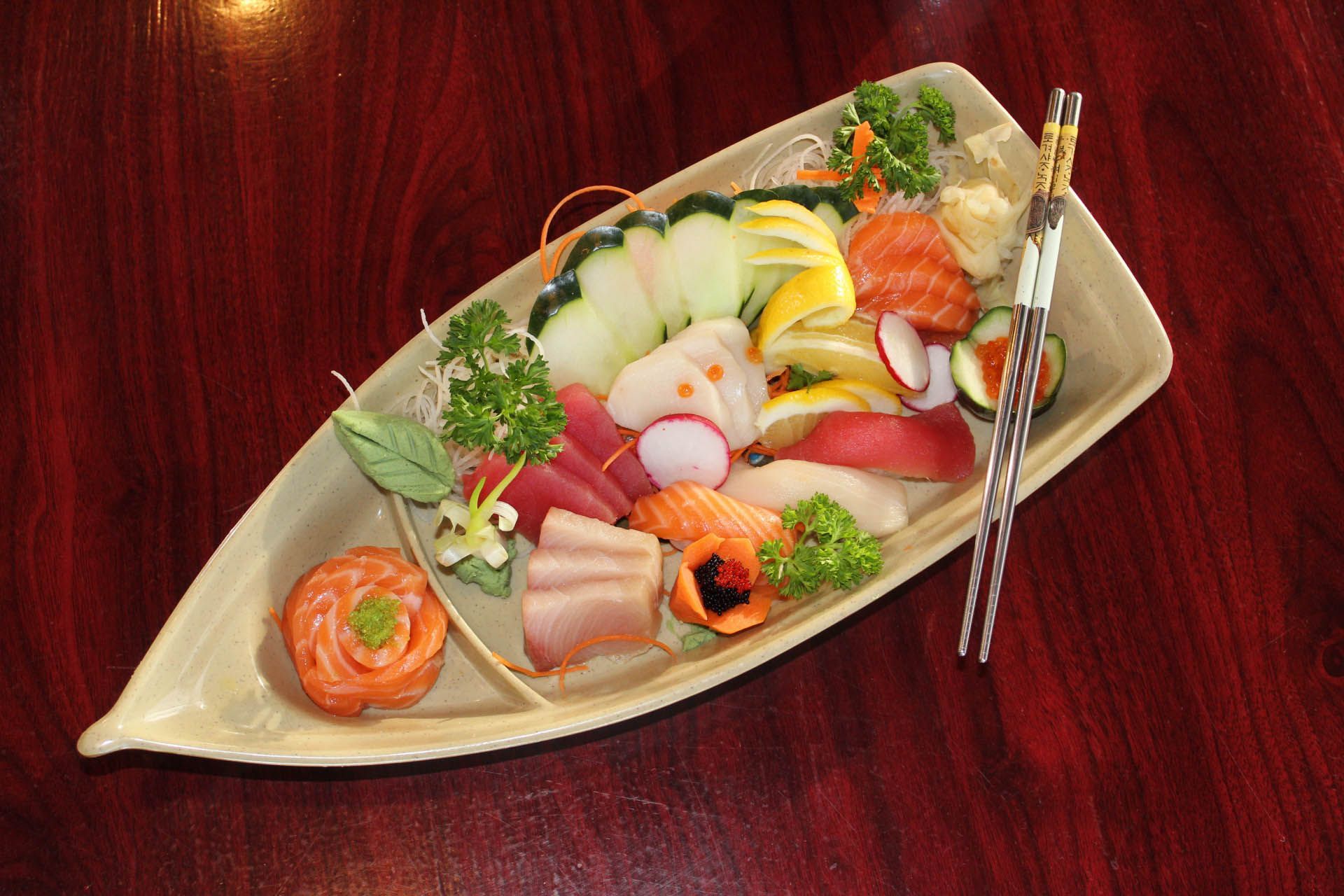 A boat shaped plate of food with chopsticks on a wooden table.