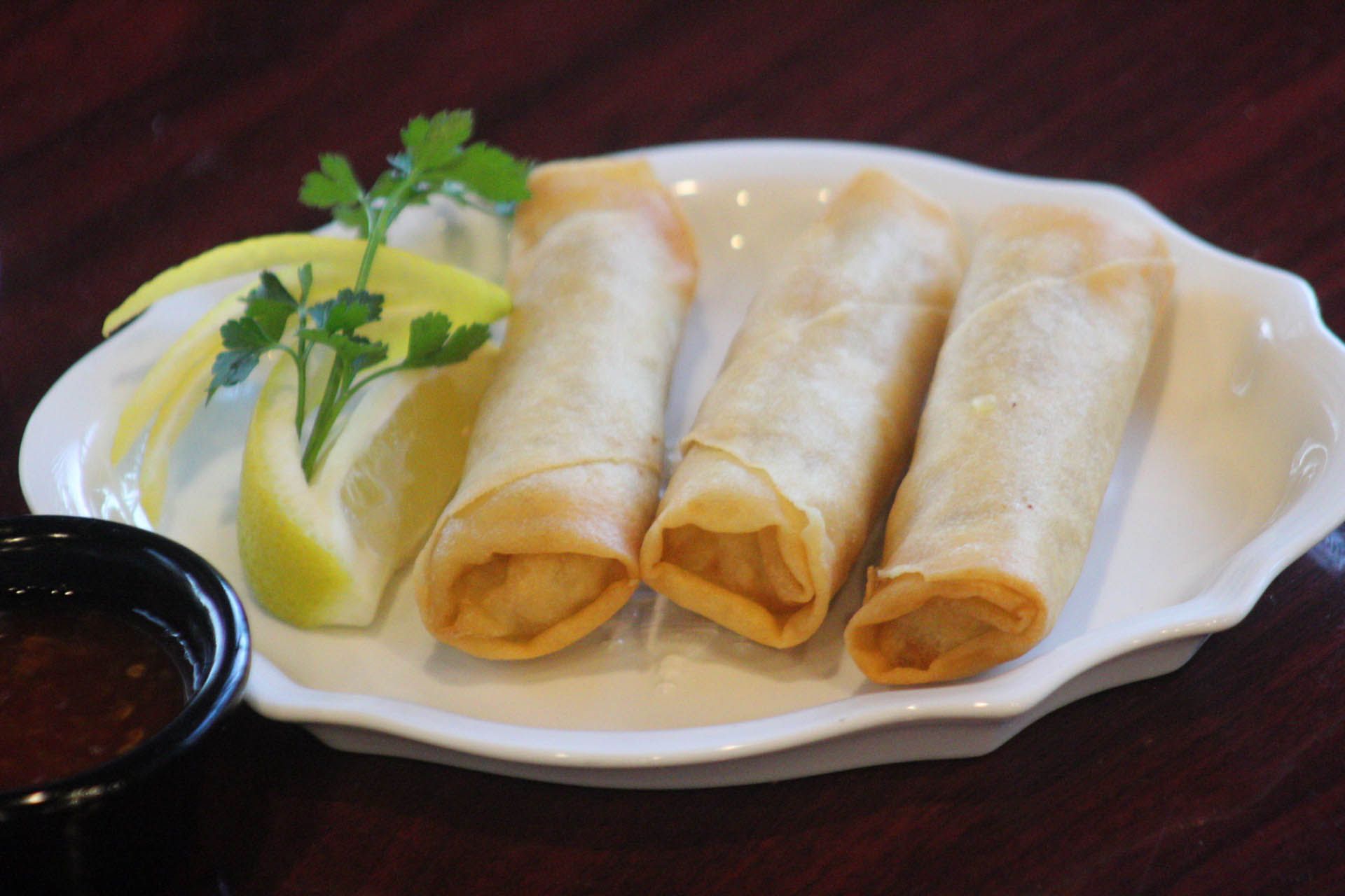 A white plate topped with three egg rolls and a slice of lemon.