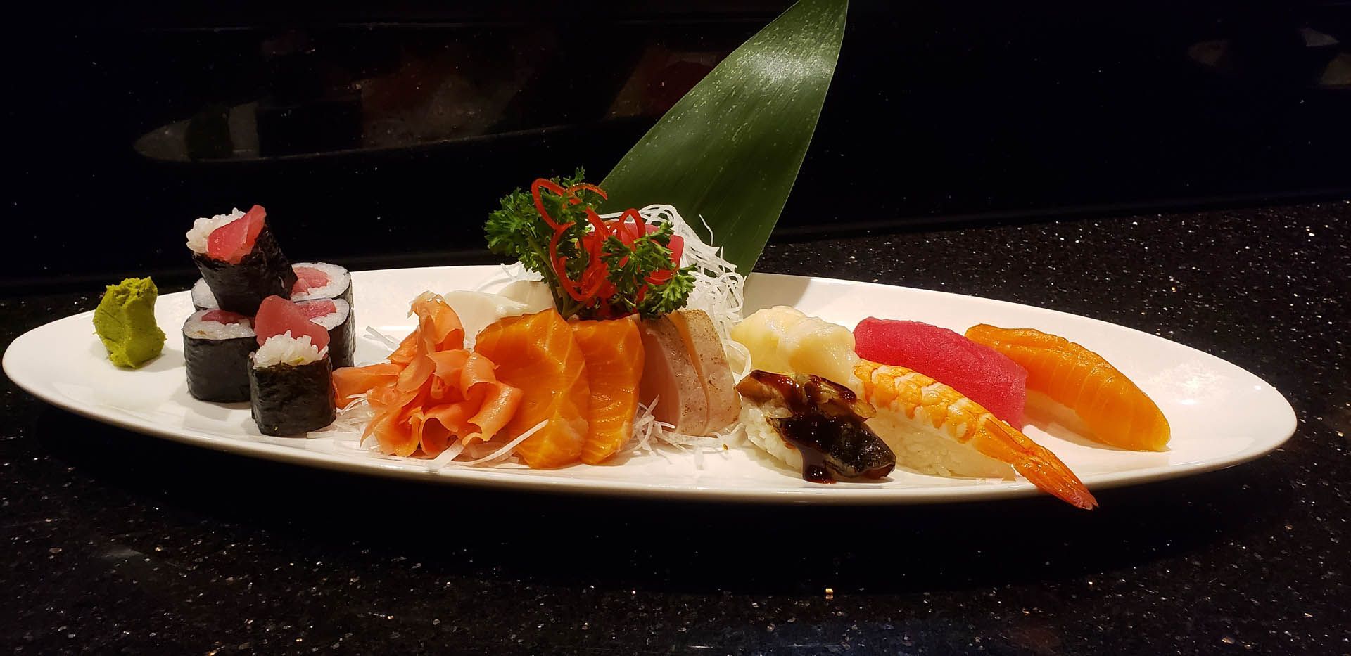 A white plate topped with sushi and fruit on a table.