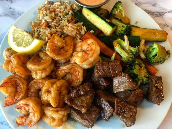 A plate of food with shrimp , steak , rice and vegetables on a table.