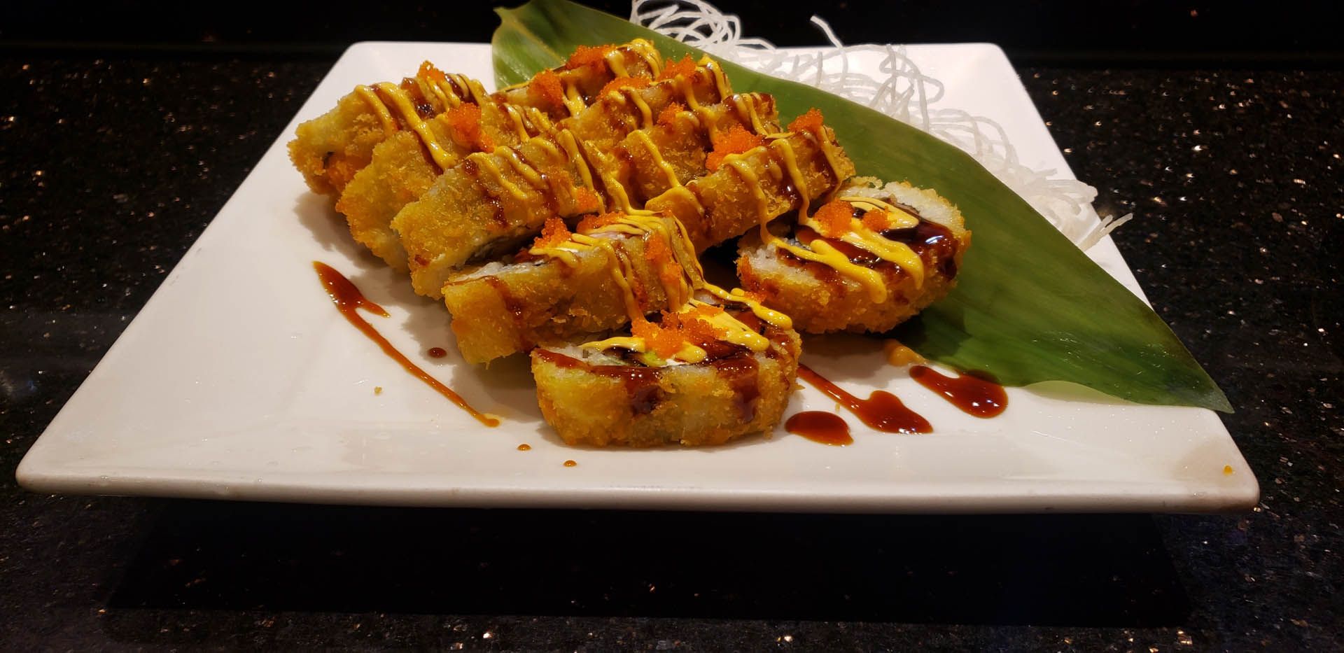 A white plate topped with fried sushi and a green leaf.