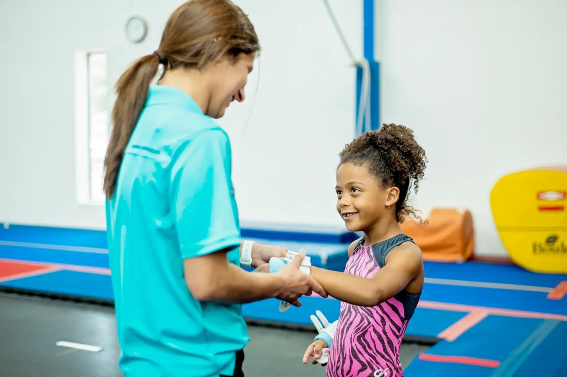 Gymnastics coach giving a child wrist supports in a gym. Both smiling.