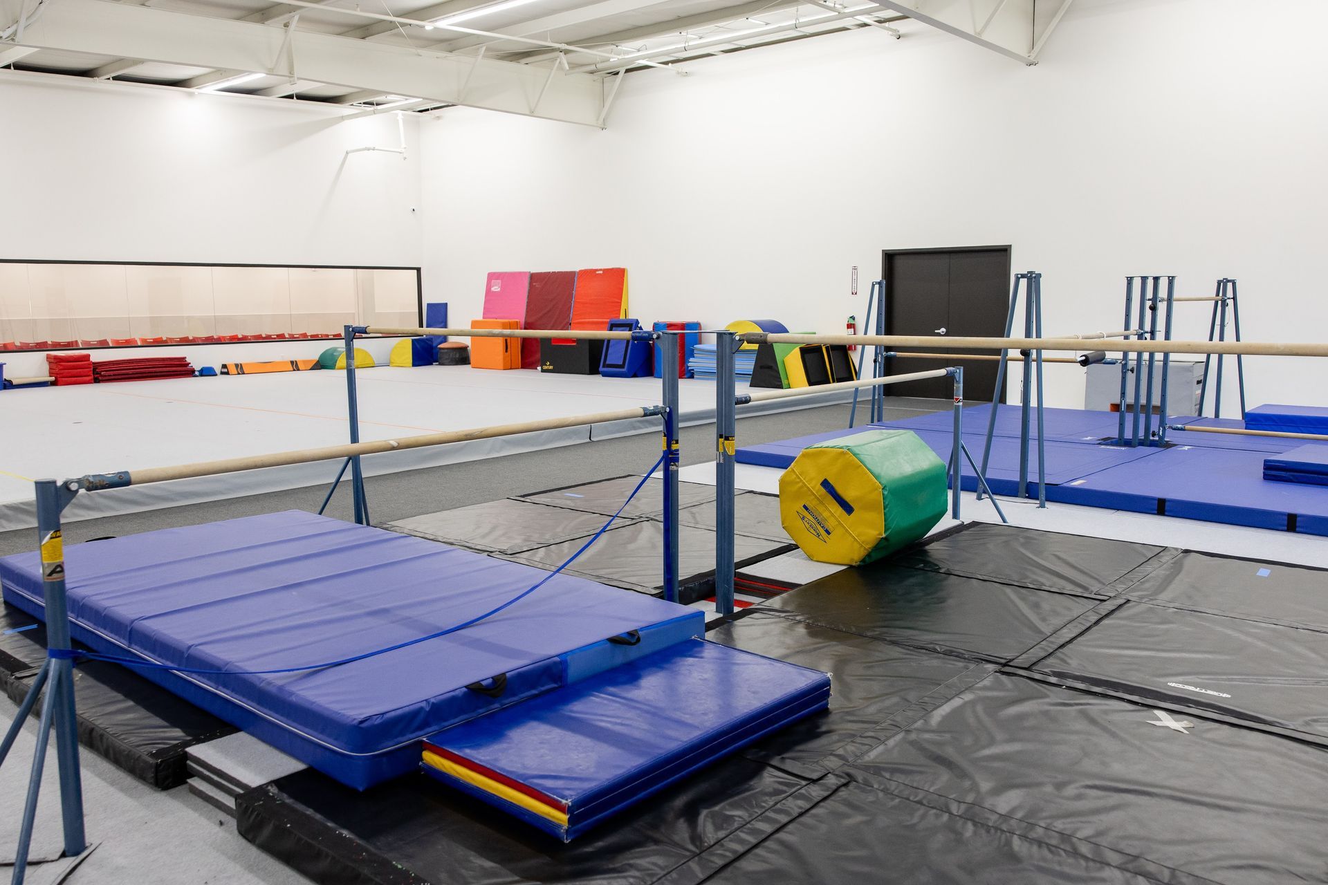 Indoor gymnastics training area with blue mats, bars, and foam equipment