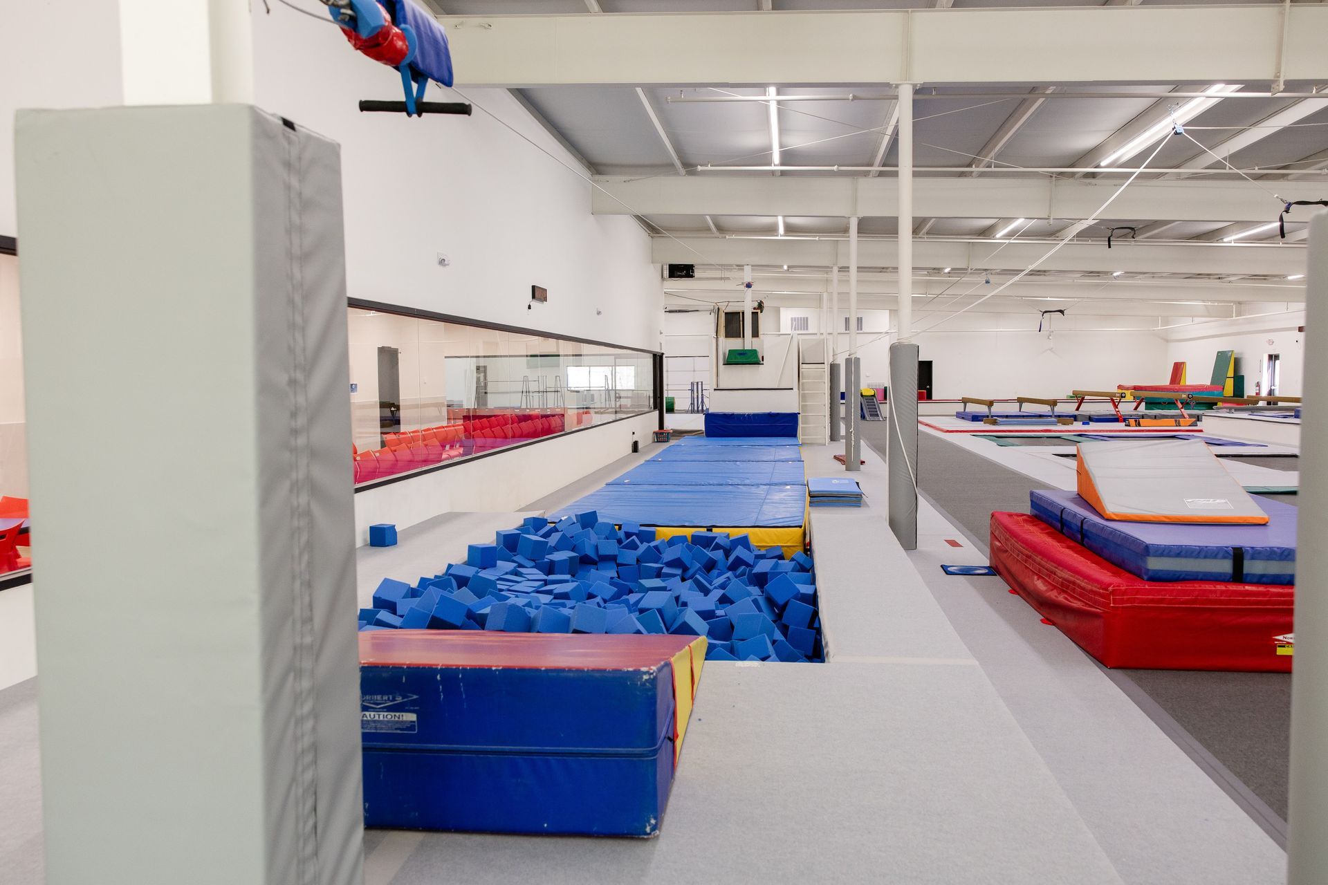 Gymnastics training area with blue foam pit, zipline, and colorful mats in an indoor gym