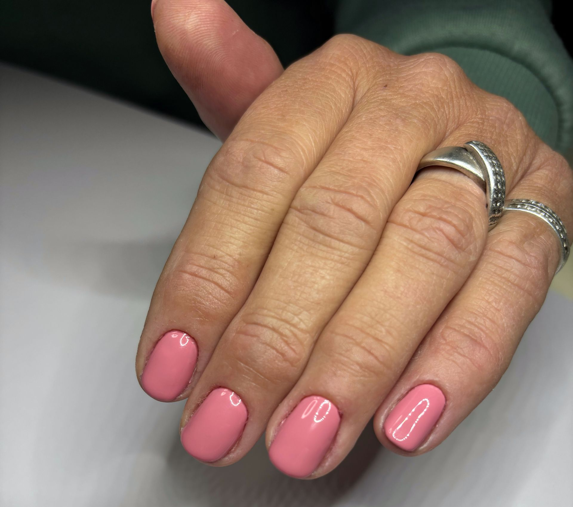 Hand met roze gelakte nagels en zilveren ringen.