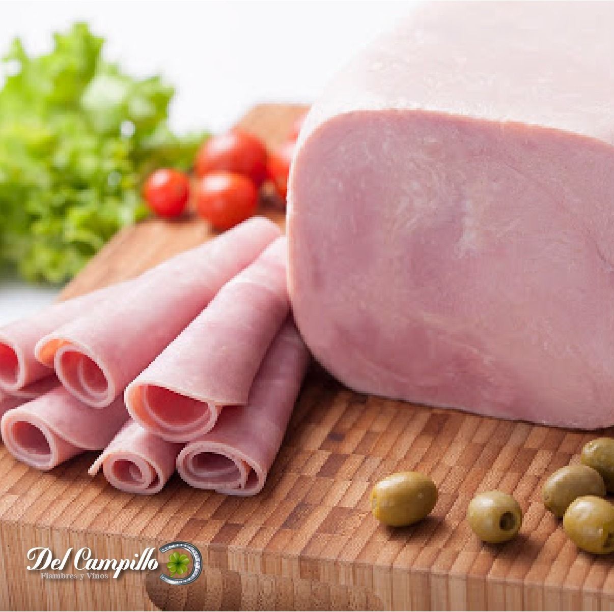 Jamón en rodajas con tomates, lechuga y aceitunas sobre una tabla de cortar de madera.