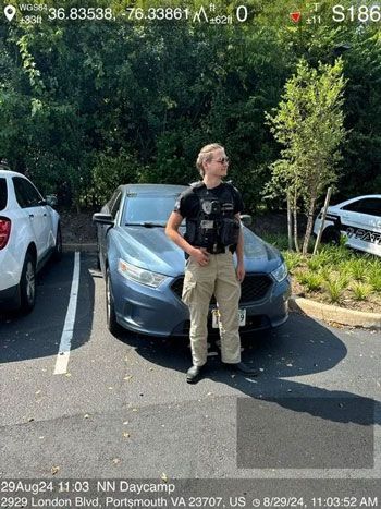 A person in uniform stands by a blue car in a parking lot, sunny day.
