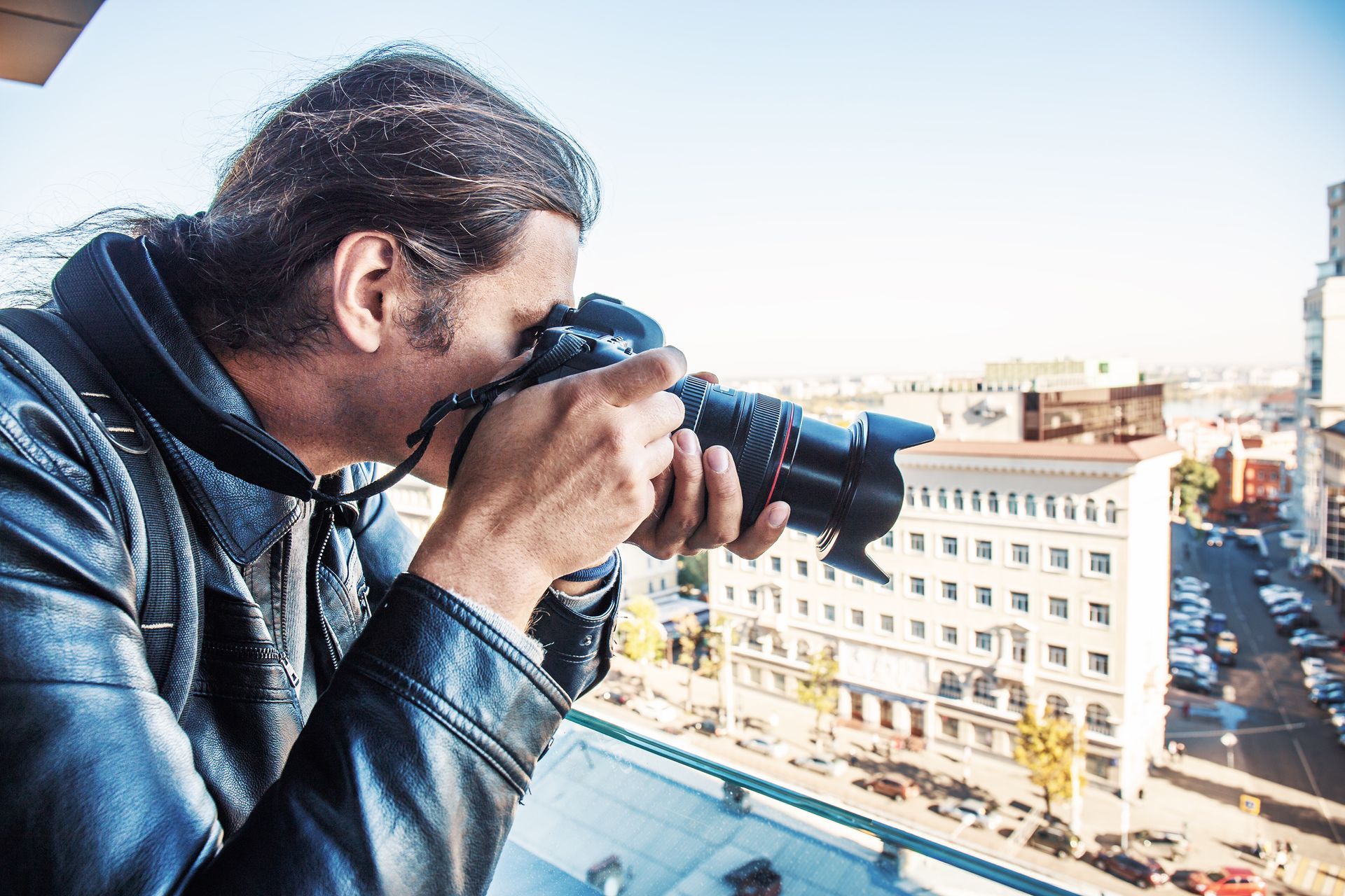 A private detective taking photos from the balcony of a building with a professional camera.