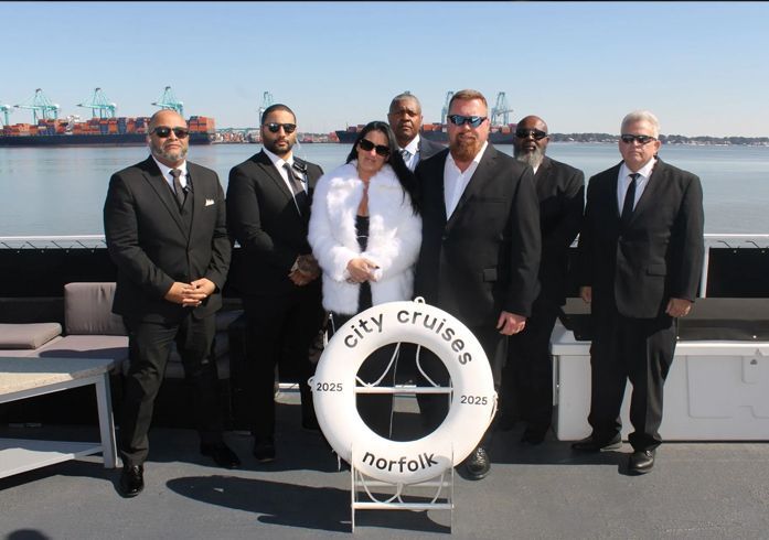 Group of people on a boat deck near Norfolk, VA, posing with a life preserver for a City Cruises event.