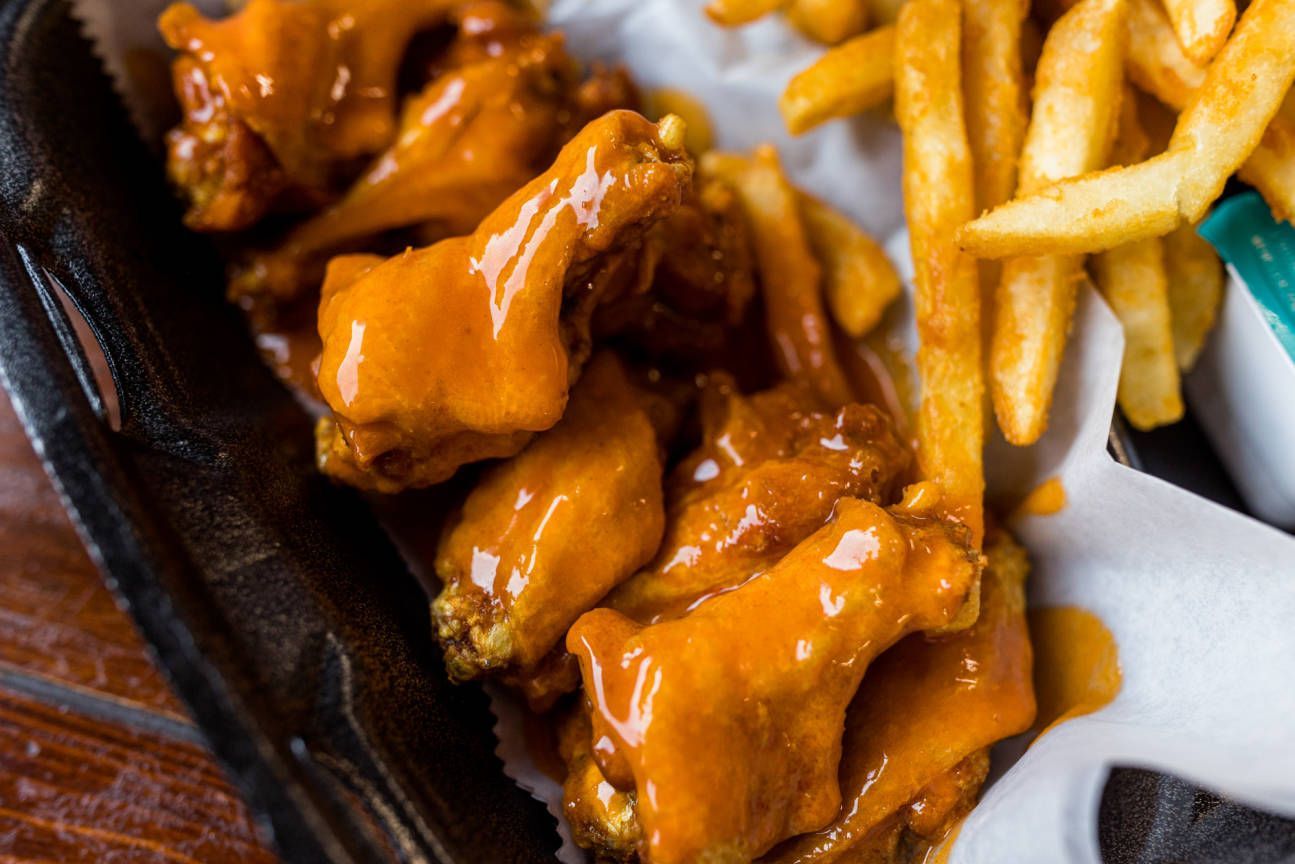 A basket of chicken wings and french fries on a table.