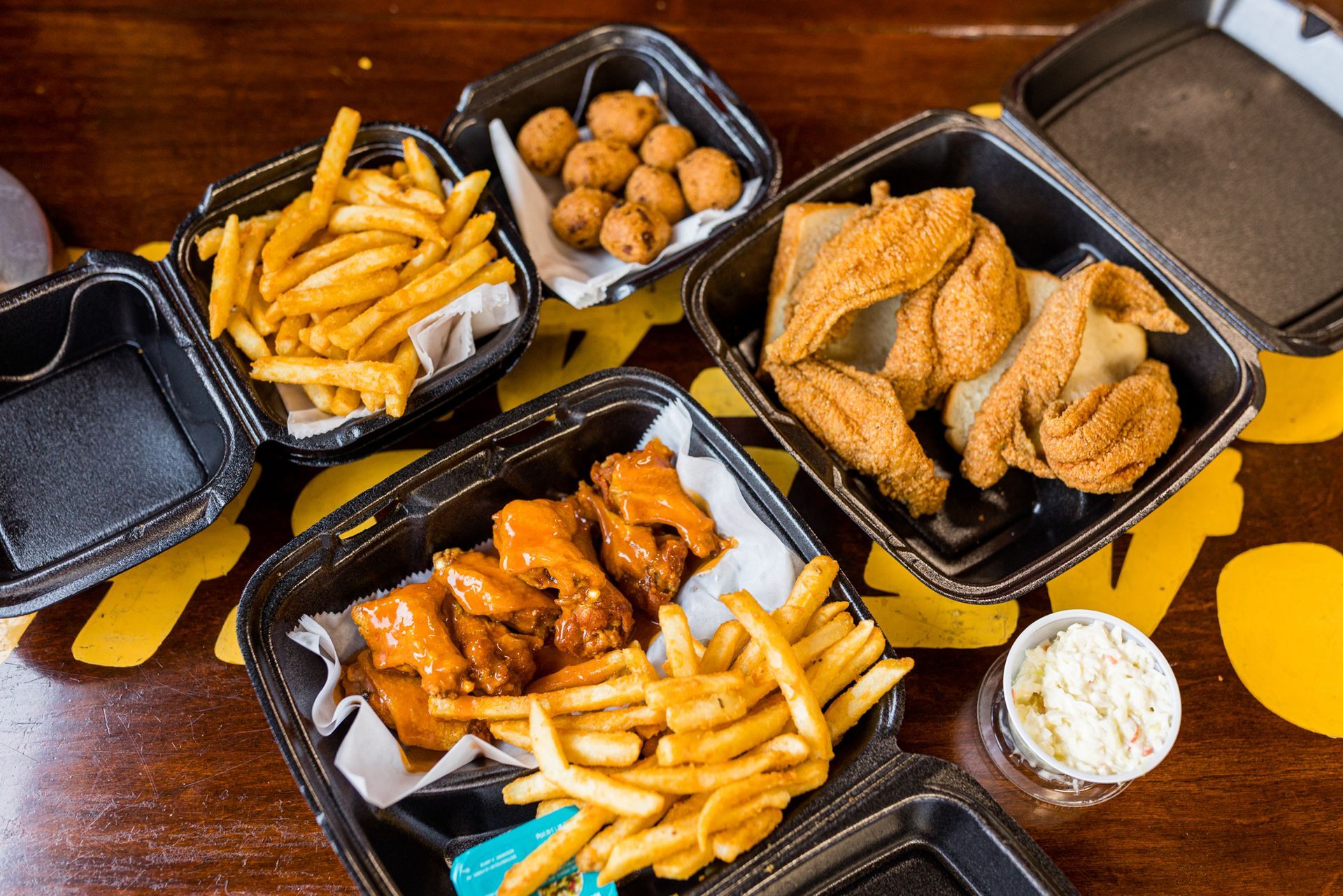 A table topped with containers of chicken wings , french fries , and coleslaw.