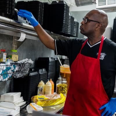 A man wearing a red apron and blue gloves is standing in a kitchen.