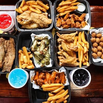 A table topped with a variety of food including french fries , chicken wings , fish , and drinks.