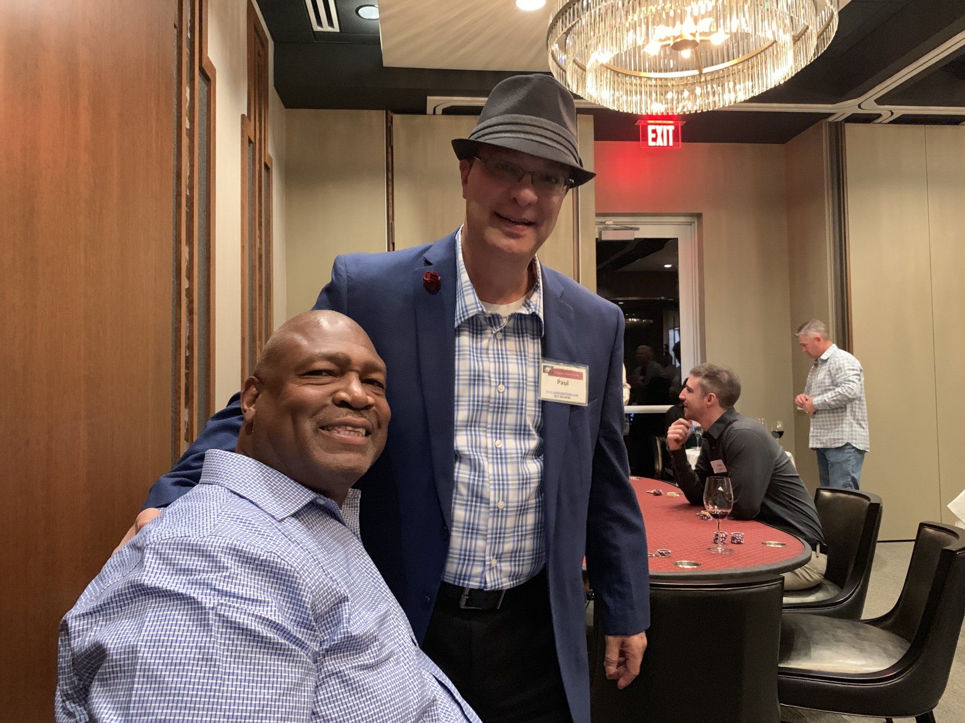 Two men are posing for a picture in a room with a red exit sign