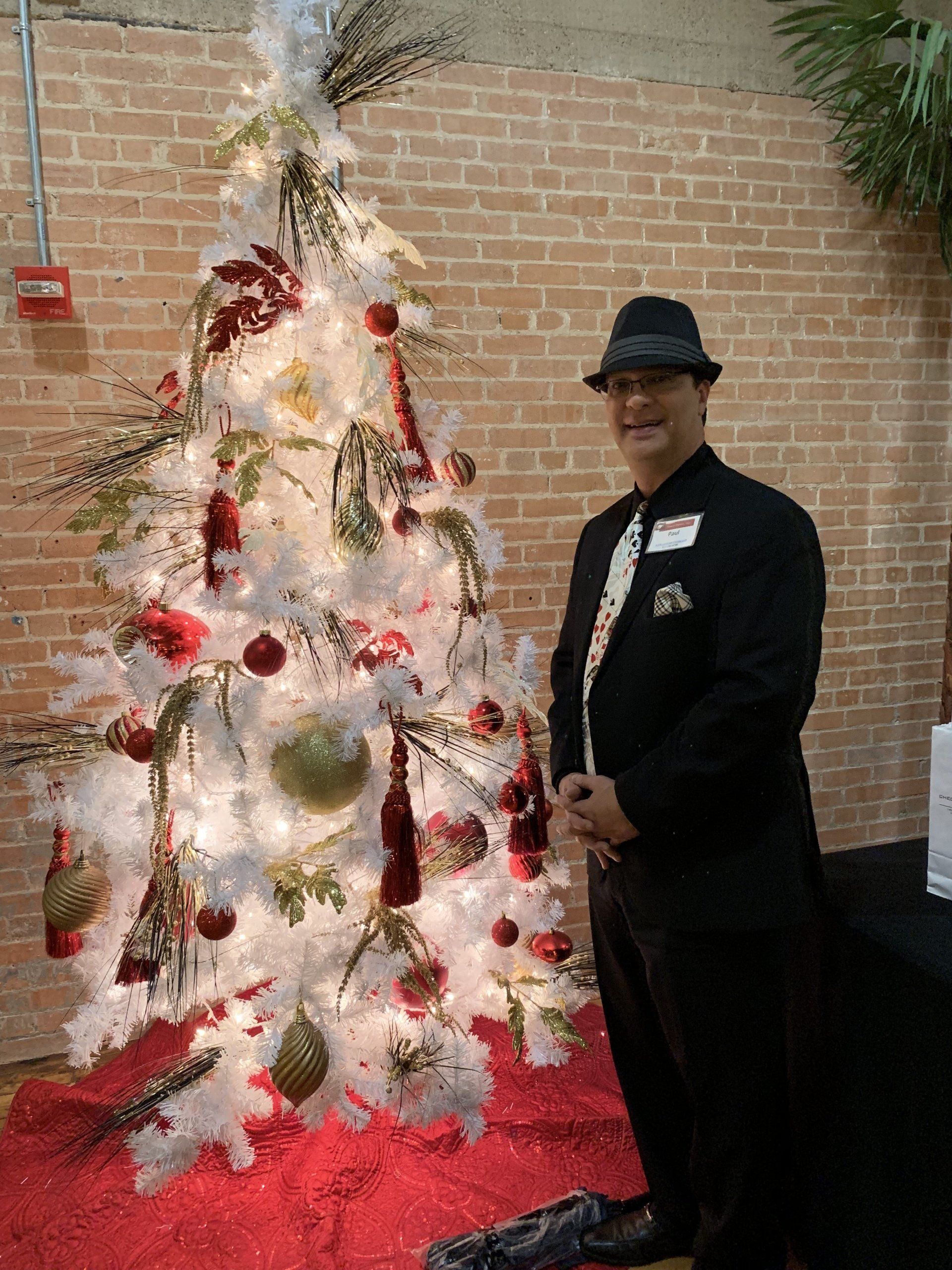 A man in a suit and hat is standing in front of a white christmas tree.