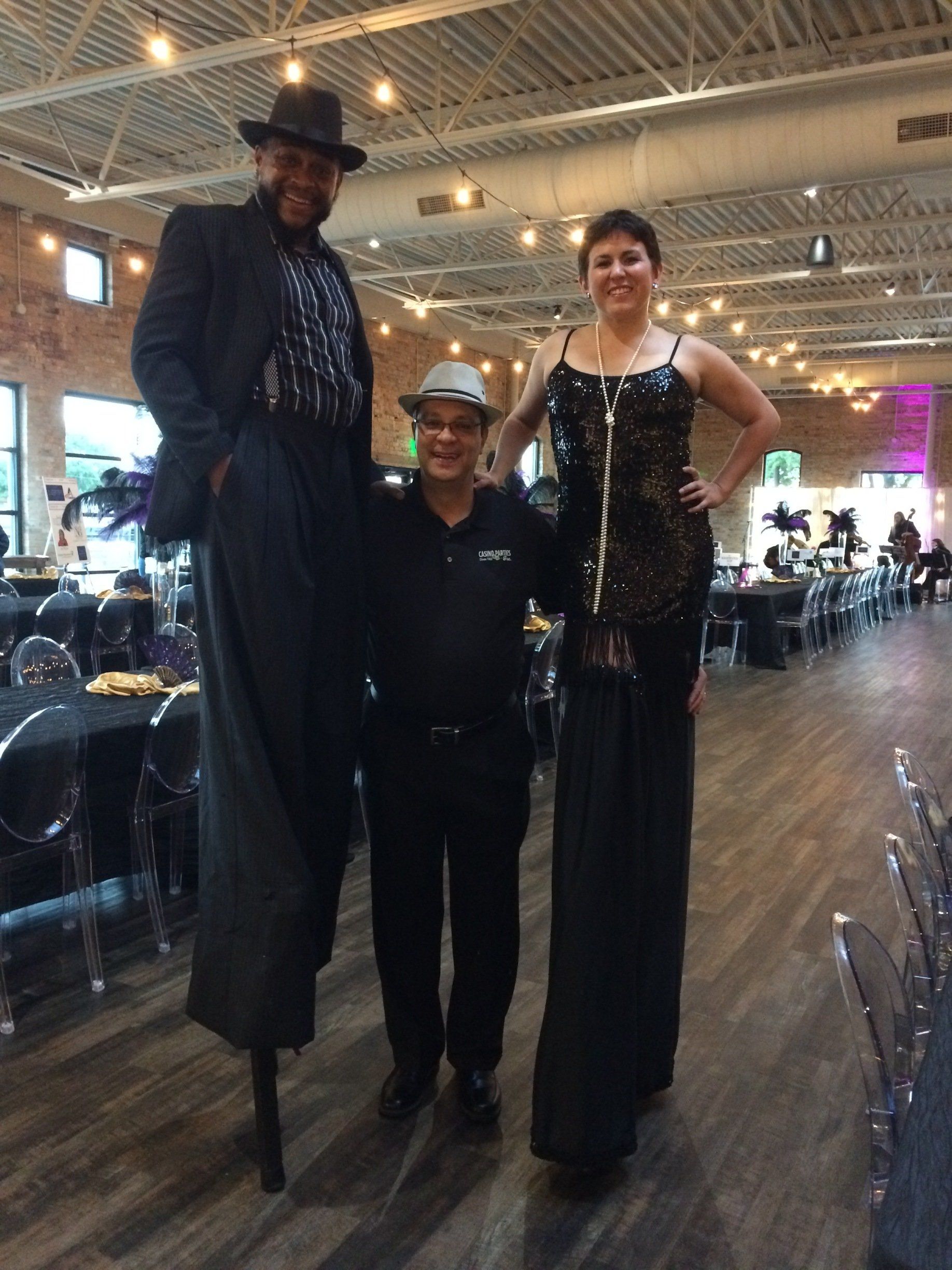 A man and two women are standing on stilts in a large room.