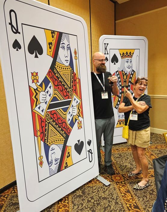 A man and a woman are standing in front of a queen spades playing card