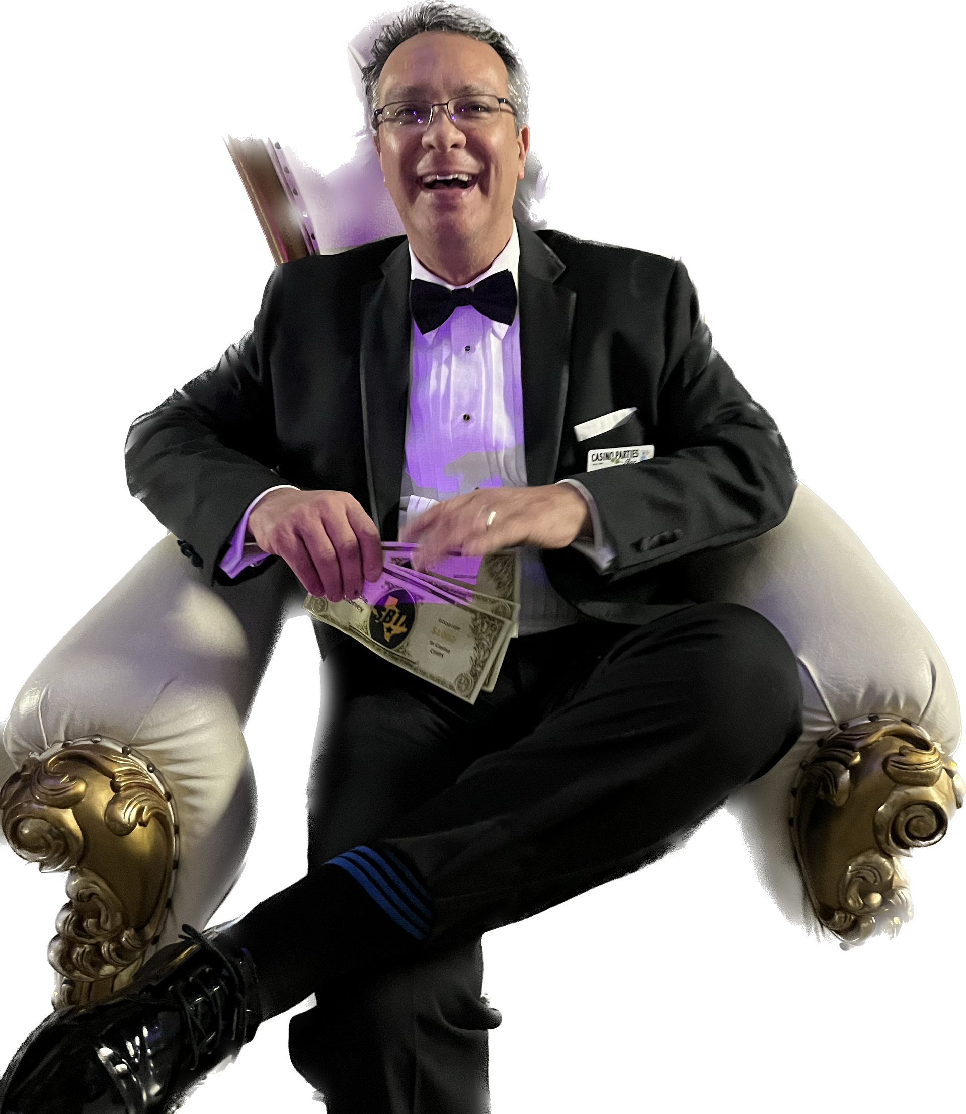 A man in a tuxedo is sitting in a chair holding a dollar bill