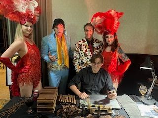 A man is sitting at a table with a group of people standing around him.