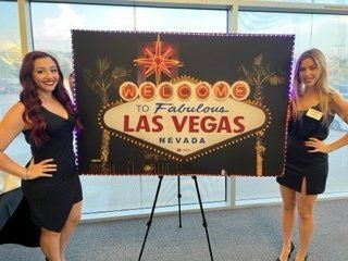Two women standing in front of a sign that says welcome to fabulous las vegas nevada
