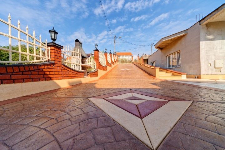 Sunlit rooftop terrace with patterned stone paving, red brick walls, and white railings under a blue sky