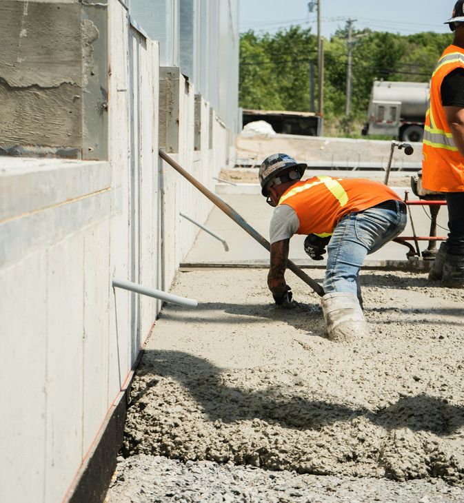 Construction worker in orange vest leveling wet concrete beside a wall on a job site
