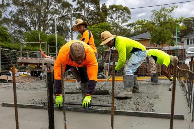 Construction workers pouring and leveling wet concrete at a building site.