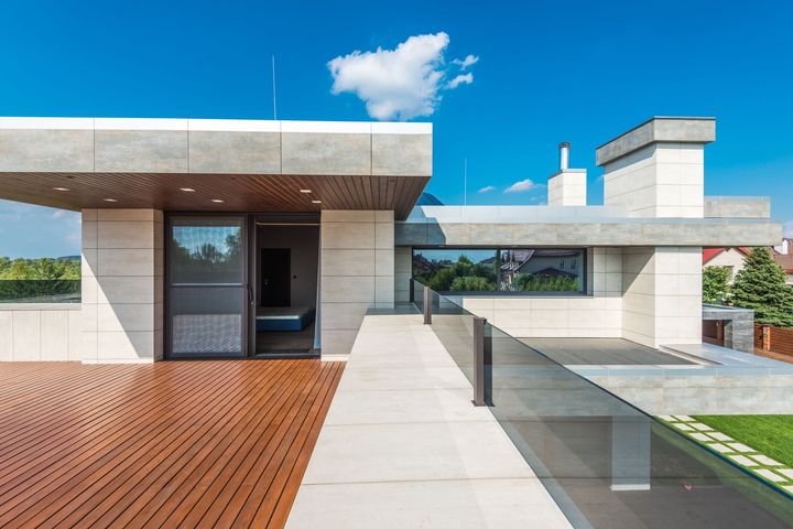 Modern rooftop terrace with wooden deck, glass railing, and concrete seating under a blue sky
