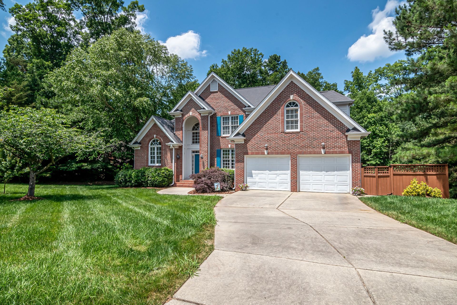 Brick suburban house with two-car garage, front lawn, and curved driveway under a blue sky