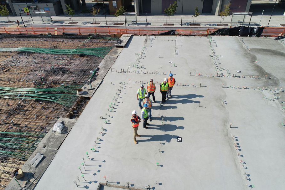 Construction workers in safety vests stand on a concrete slab at a building site.