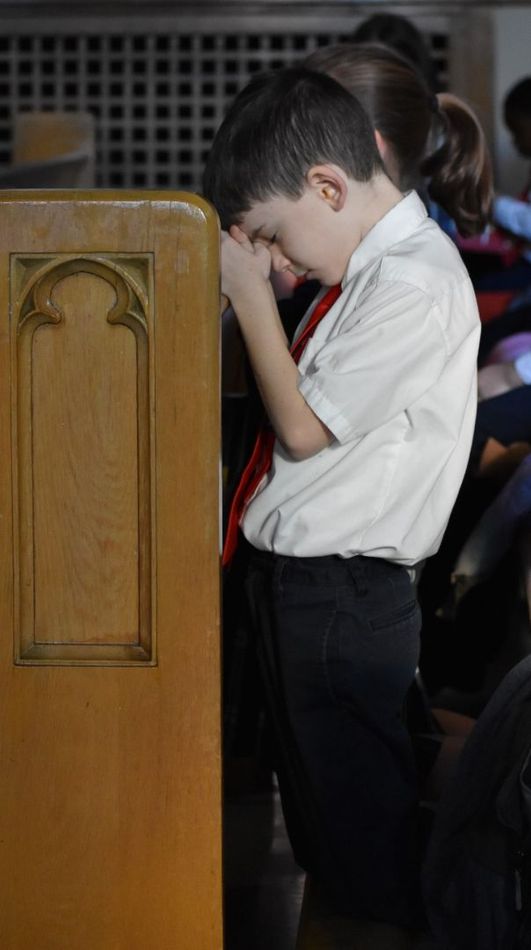 A young boy praying in a church with his hands folded