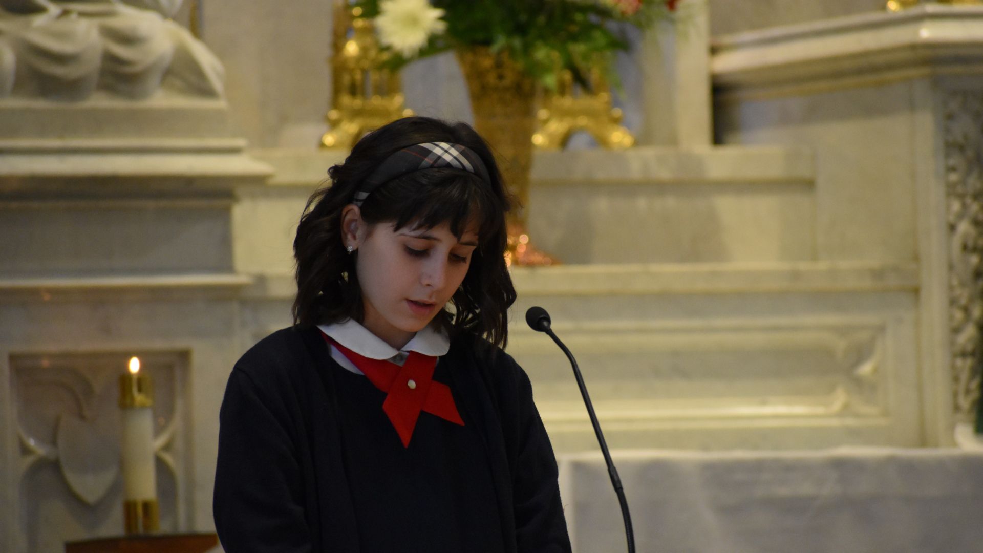 A young girl stands in front of a microphone in a church