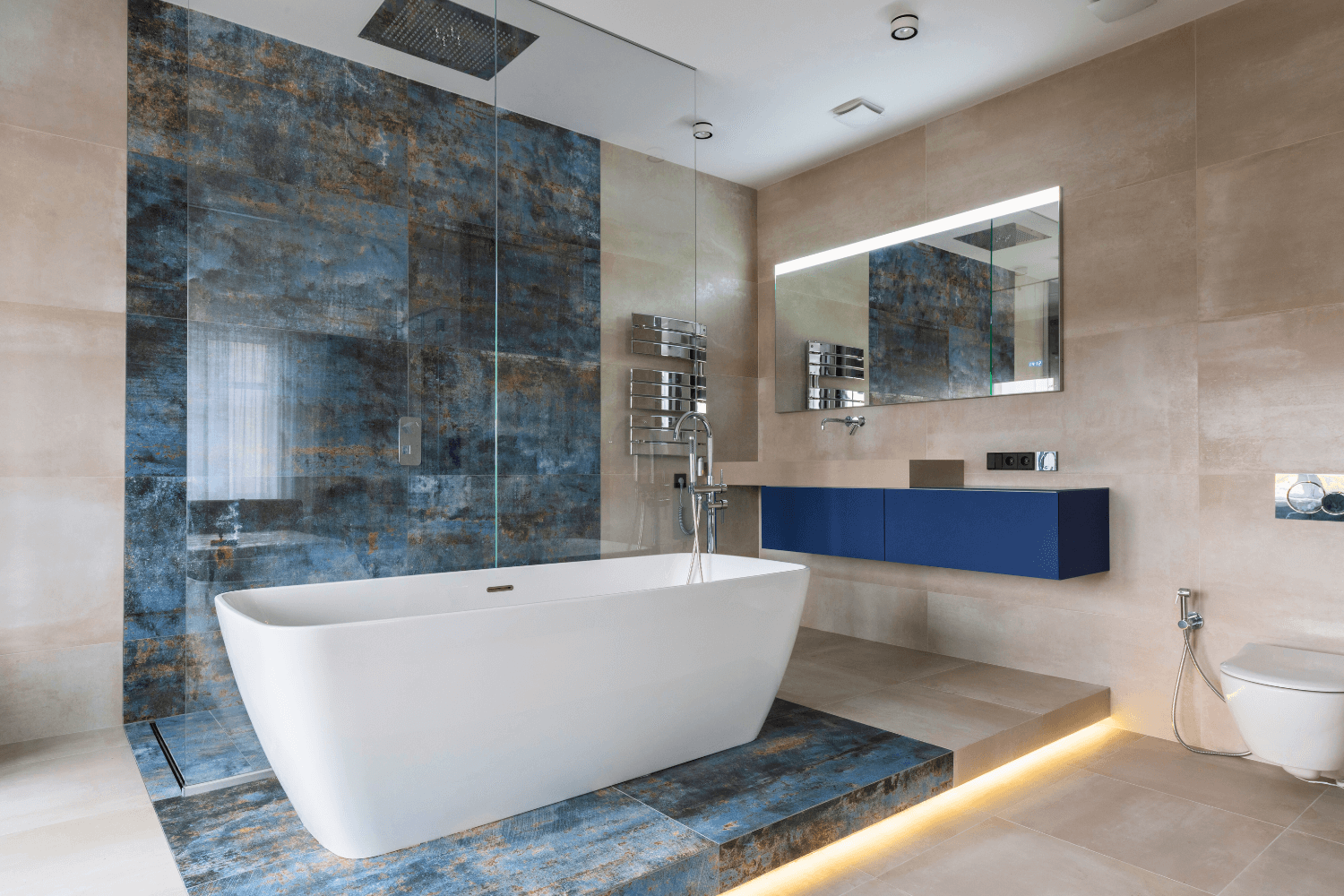 Baño moderno con bañera blanca, pared decorativa azul y tocador flotante azul.