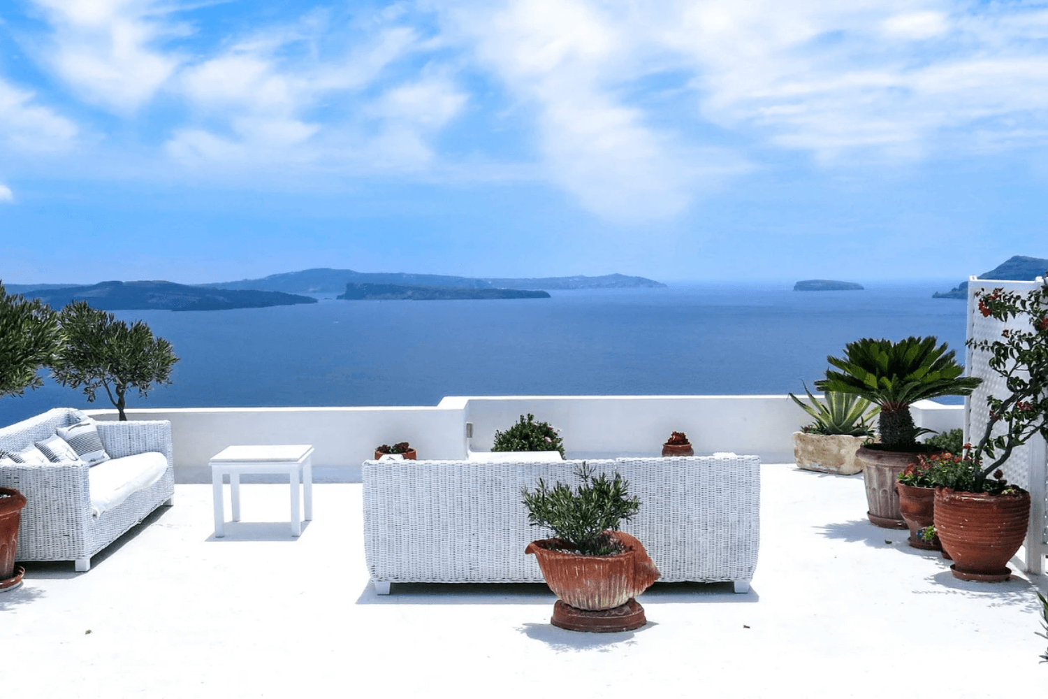 Muebles de patio blancos con vistas al mar Egeo en Santorini, Grecia. Cielo azul brillante y océano.