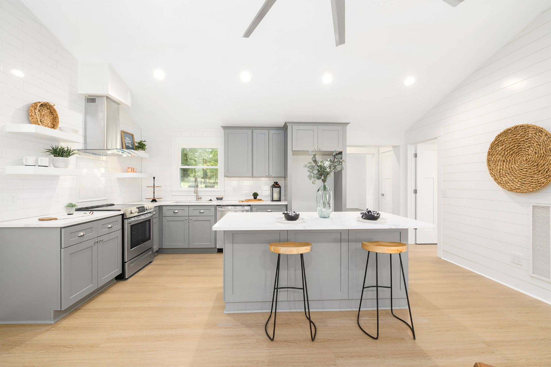 Cocina gris moderna con encimeras blancas, una isla central con taburetes y pisos de madera clara.