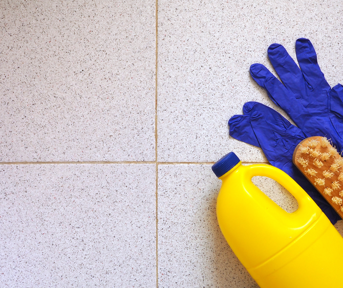 Yellow bleach bottle, blue gloves, and scrub brush on a tiled floor.