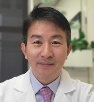 Dr. Suh in a white coat and tie is smiling for the camera.