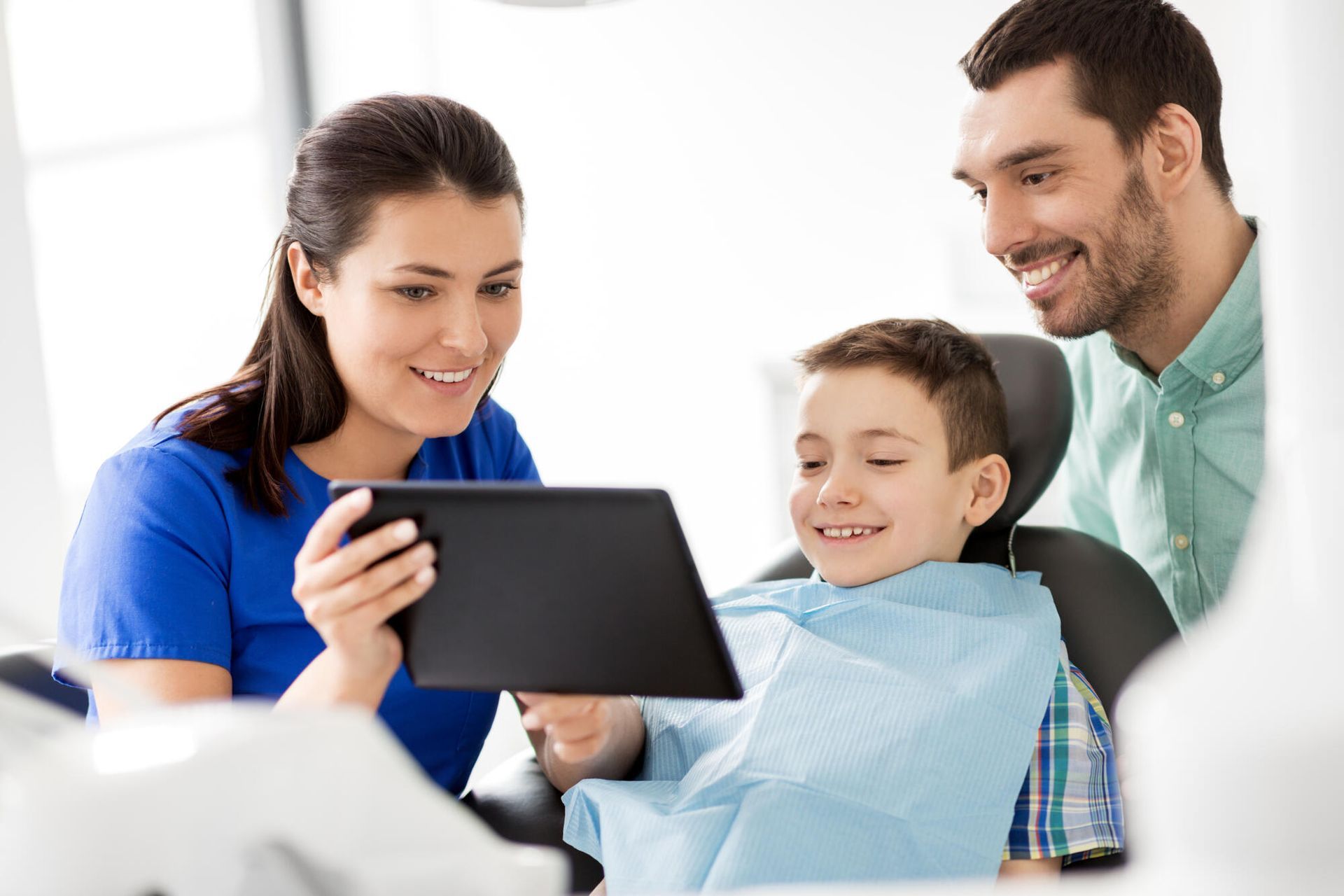 A man and woman are looking at a tablet with a child in a dental chair.