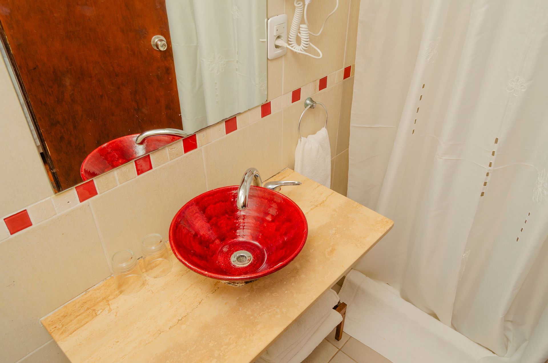 Un lavabo de color rojo brillante descansa sobre una encimera de madera clara en un baño con espejo de pared y cortina de ducha blanca.