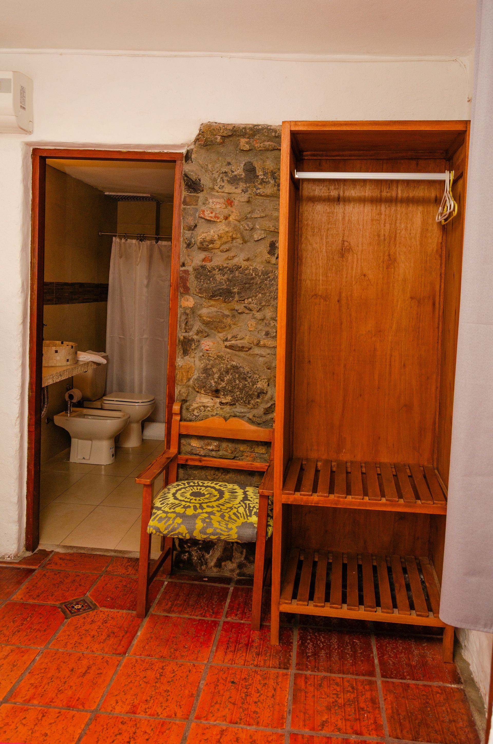 Una puerta de baño, una silla de madera con un cojín estampado y una estantería abierta de madera con una barra para colgar la ropa.