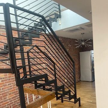 A black metal staircase in a living room with a brick wall.